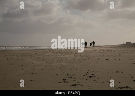 Vier Menschen zu Fuß entlang einem einsamen Strand an der Küste von Norfolk im winter Stockfoto