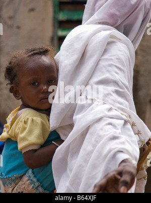 Eine Fulbe-Frau in Ouagadougou, Burkina Faso geht vorbei an der Kamera mit ihrem Kleinkind auf dem Rücken in traditionelle afrikanische Mode. Stockfoto