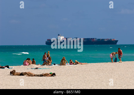 Menschen entspannen am Strand mit Containerschiff vorbei hinter South Beach Miami Gold Coast Florida Vereinigte Staaten von Amerika Stockfoto