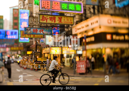 Ein Mann reitet seinen Zyklus entlang ein Kowloon Bezirk Straße beleuchtet von Neonröhren in Hong Kong Stockfoto