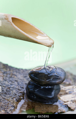 Hölzerne Tülle strömenden Wasser über Stapel von Steinen Stockfoto