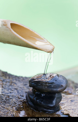 Bambus Tülle strömenden Wasser auf Stapel von Steinen Stockfoto
