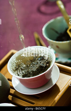 Warmwasser wird gegossen und Spritzwasser über Teeblätter in Teetasse Stockfoto