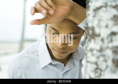 Mann gelehnt Baumstamm mit Kopf ruht auf Arm, Augen geschlossen Stockfoto