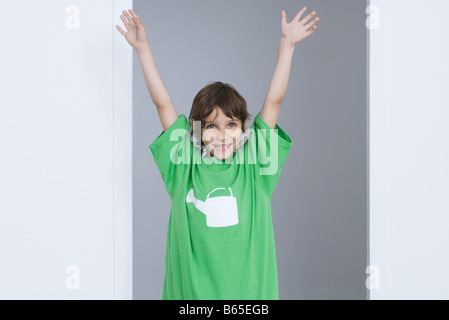 Jungen tragen übergroße t-Shirt mit Gießkanne aufgedruckt, Arme in die Luft heben lächelnd Stockfoto