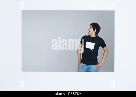 Junger Mann mit t-Shirt bedruckt mit leeren Wort Blase, Hände schreien, auf den Hüften Stockfoto