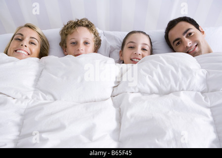 Familie liegen zusammen im Bett unter Tröster, lächelnd in die Kamera Stockfoto