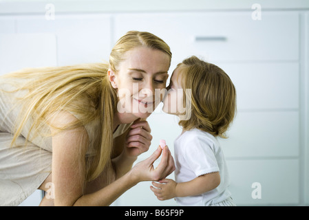 Kleine Mädchen küssen Mutter Backe, Frau hält ein kleines Herz, Augen geschlossen Stockfoto