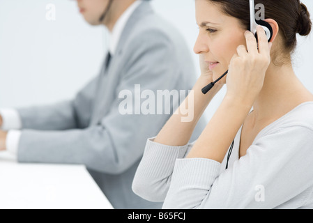 Berufstätige Frau, Kopfhörer, männlicher Kollege im Hintergrund, Seitenansicht anpassen Stockfoto