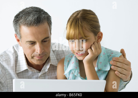 Vater und Tochter mit Blick auf Laptop-Computer zusammen, der Mensch ist Arm um Mädchen auf die Schulter Stockfoto