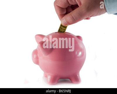 Energiesparmodus. Eine Sparer Einlagen eine wertvolle Goldbarren Bar in ein Sparschwein. Isoliert auf weißem Hintergrund. Stockfoto