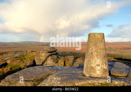 Licht des frühen Morgens und ein Regenbogen am Bellever Tor auf Dartmoor in South Devon UK mit der Triangulation Säule auf dem Gipfel Stockfoto