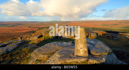 Licht des frühen Morgens und ein Regenbogen am Bellever Tor auf Dartmoor in South Devon UK mit der Triangulation Säule auf dem Gipfel Stockfoto