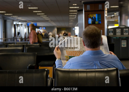 Mann wartet auf Flug, liest Zeitung im Flughafen Stockfoto