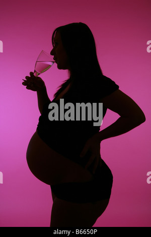 38 Woche schwangere Silhouette vor einem rosa Hintergrund aus einem Glas Wein zu trinken. Stockfoto