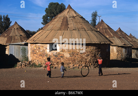 Eritreische Jungs spielen mit einem Reifen oder mit dem Fahrrad Reifen außerhalb des runden Haus oder Hütte, Asmara, Eritrea Stockfoto