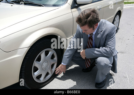 Ein Mann verkleidet für ein Geschäftstreffen, einen Platten Reifen an seinem Auto entdecken Stockfoto