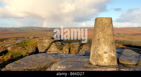 Licht des frühen Morgens und ein Regenbogen am Bellever Tor auf Dartmoor in South Devon UK mit der Triangulation Säule auf dem Gipfel Stockfoto