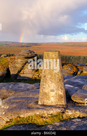 Licht des frühen Morgens und ein Regenbogen am Bellever Tor auf Dartmoor in South Devon UK mit der Triangulation Säule auf dem Gipfel Stockfoto