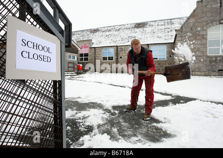 Arbeiter mit Schaufel löscht Wege außerhalb einer Schule, die in Aberdeenshire, Schottland im Winter wegen Schnee geschlossen ist Stockfoto
