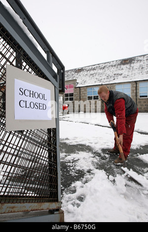 Arbeiter mit Schaufel löscht Wege außerhalb einer Schule, die in Aberdeenshire, Schottland im Winter wegen Schnee geschlossen ist Stockfoto