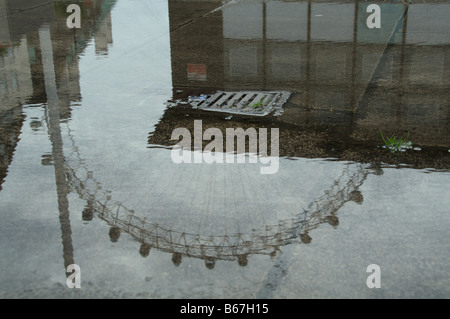 London Eye spiegelt sich in einer Pfütze des Regenwassers, spiegelt das typische London-Wetter Stockfoto