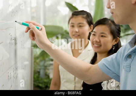 Nahaufnahme von einer männlichen Büroangestellten auf einem Whiteboard schreiben und zwei weibliche Büroangestellte, die es auf Stockfoto