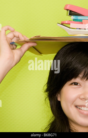 Porträt einer jungen Frau Büro Papeterien auf dem Kopf tragen und lächelnd Stockfoto