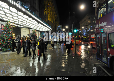 Oxford Street Verkehr & Shopper mit Weihnachtsdekoration im Regen vor Selfridges Kaufhaus Haupteingang West End London England Großbritannien Stockfoto