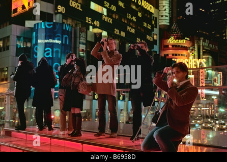 Broadway Lichter lodern hinter Touristen wie sie des Times Square, New York, Vereinigte Staaten fotografieren Stockfoto