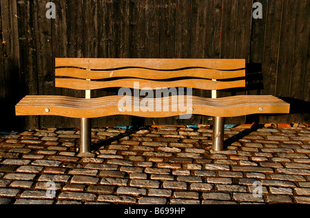 Eine öffentliche Holzbank im Hafen. Die welligen Formen davon erinnern an das Meer. Stockfoto