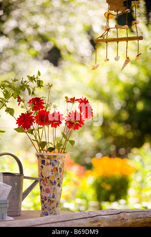 Gießkanne mit einer Vase mit Blumen und einem Windspiel Stockfoto