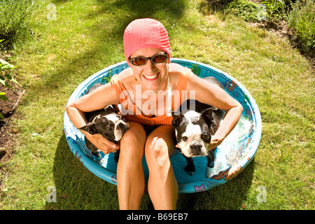 Frau sitzt in einem Planschbecken mit zwei Boston Terrier Stockfoto