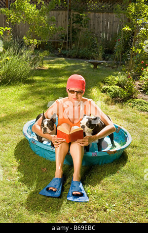 Frau liest ein Buch in einem Planschbecken zwischen zwei Boston Terrier Stockfoto