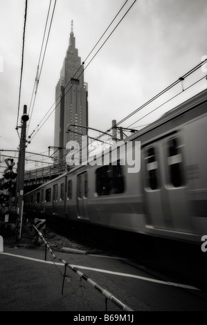 NTT DoCoMo Yoyogi Gebäude (Hintergrund) und einen Zug in Bewegung auf einer Straße über Bahnübergang. Shinjuku. Tokyo. Japan. Stockfoto