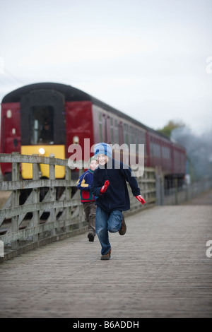 Zwei jungen laufen neben einen Zug auf einer Eisenbahnlinie Erbe in Northamptonshire MODEL RELEASE verfügbar Stockfoto