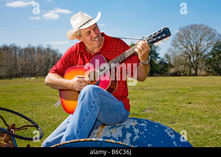 Schöne Reife Cowboy seine Gitarre spielen und singen beim Sitzen auf seinem Traktor Stockfoto