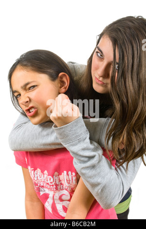 Vertikale Nahaufnahme Portrait eine große Schwester mit ihrer kleinen Schwester in einem Headlock mit einem Kampf gegen einen weißen Hintergrund. Stockfoto