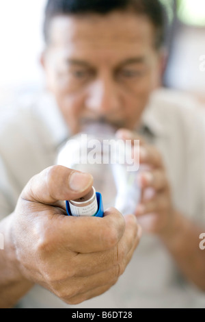 Asthma-Abstandhalter-Einsatz. Mann mit einer Asthma-Abstandhalter mit einer blauen Asthma-Inhalator. Stockfoto