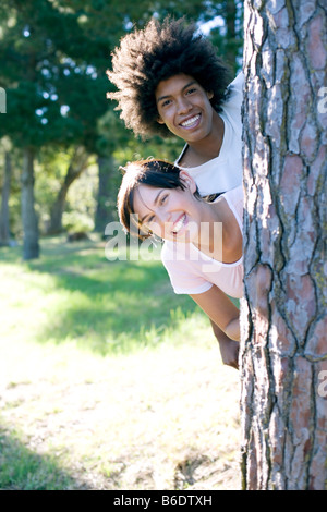 Junge Frau und Mann schaut hinter einem Baumstamm Stockfoto