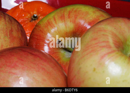 Vier Äpfel und eine Orange in einem roten Schüssel noch Leben Stockfoto