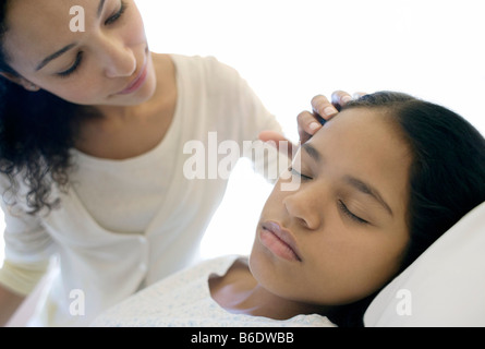 Besuch im Krankenhaus. Mutter ihre Tochter Haar streicheln, als sie in einem Krankenhausbett schläft. Stockfoto