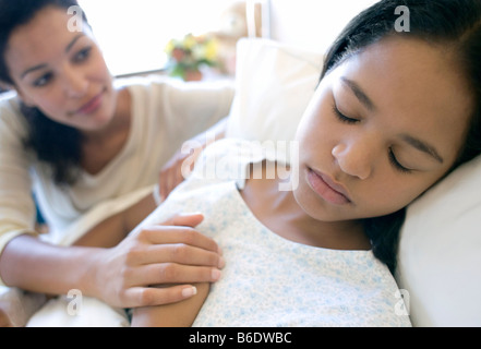 Besuch im Krankenhaus. Mutter ihre Tochter Haar streicheln, als sie in einem Krankenhausbett schläft. Stockfoto