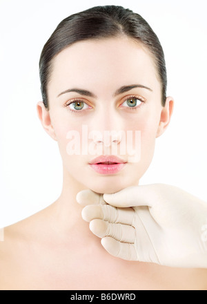 Kosmetische Chirurgie. Konzeptbild der kosmetischen Chirurgie durch eine behandschuhte Hand berühren das Gesicht einer Frau vertreten. Stockfoto