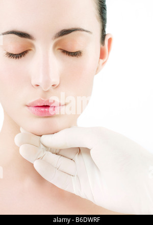 Kosmetische Chirurgie. Konzeptbild der kosmetischen Chirurgie durch eine behandschuhte Hand berühren das Gesicht einer Frau vertreten. Stockfoto