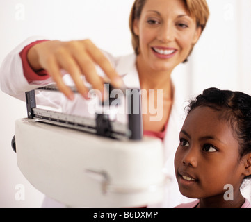 Gewichts-Check-Up. Allgemeinmedizin Arzt beobachten ihre 9 jährige Patientin die Balance auf die Waage. Stockfoto