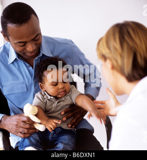 Pädiatrische Untersuchung. Arzt untersucht einen 5 Monate alten Jungen in des Vaters Schoß sitzen. Stockfoto