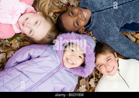 Lächelnde Mädchen und Jungen auf Herbstlaub liegend. Stockfoto