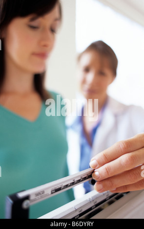 Gewichts-Check-Up, allgemeine Praxis Arzt einstellen der Balance auf Waagen beim Wiegen einer jungen Patientin Stockfoto