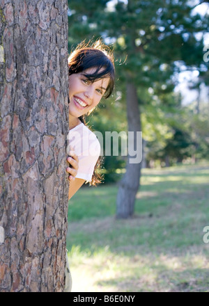 Glückliche Frau schaut hinter einem Baum. Stockfoto